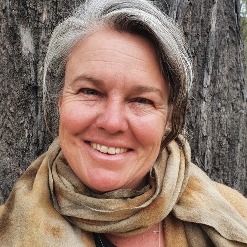 A woman with grey hair and earing earthy colours smiling at camera